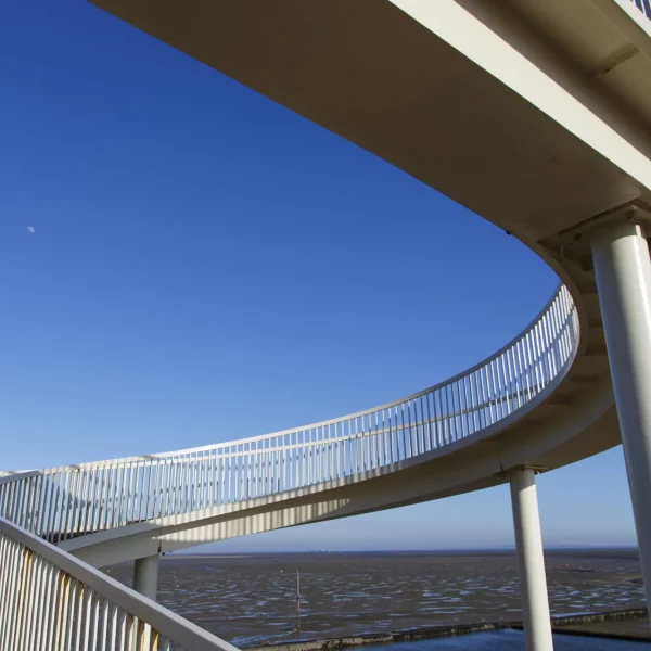 Curving white ramps and railings of Gypsy Bridge in Chalkwell, with blue sky and the shoreline beyond