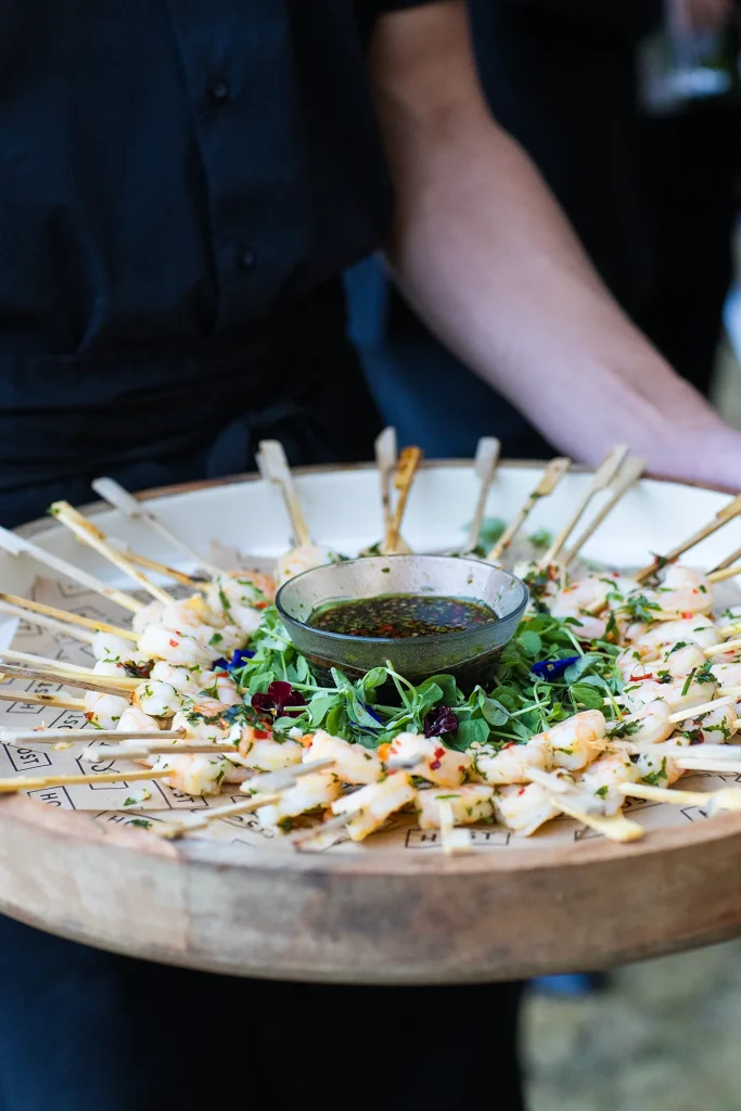 A server holds a round platter of skewered canapés around a central bowl of dip
