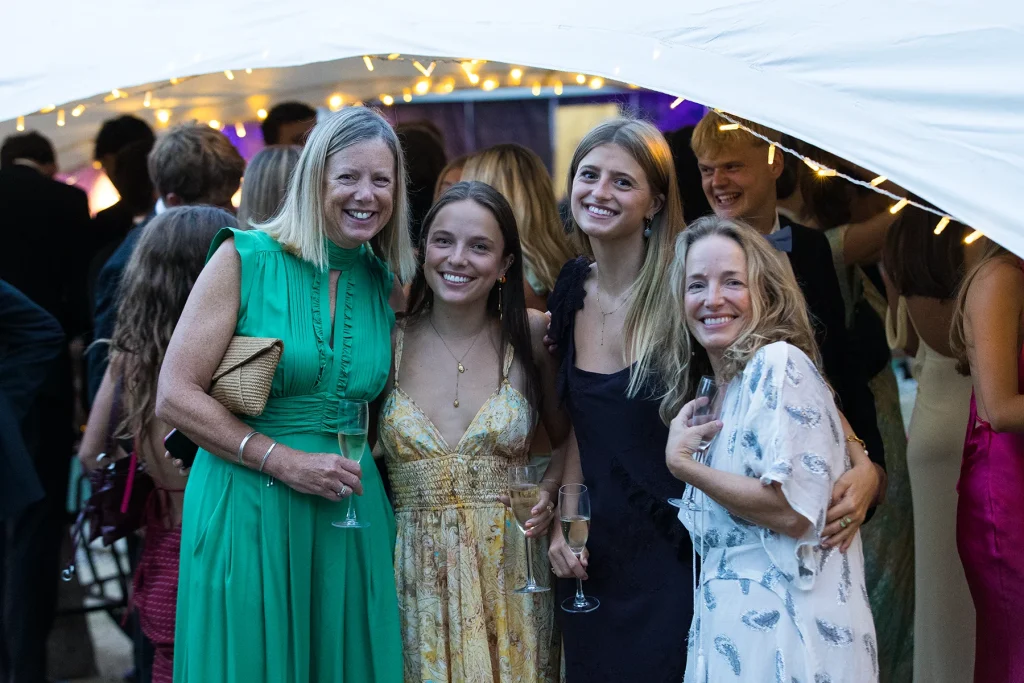 Four smiling guests stand with their arms around one another beside the lit marquee entrance