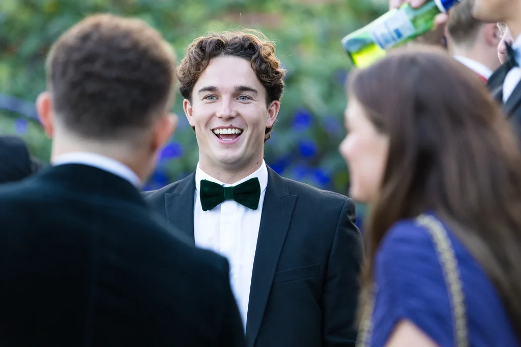 A laughing guest wearing a green bow tie talks with others outdoors