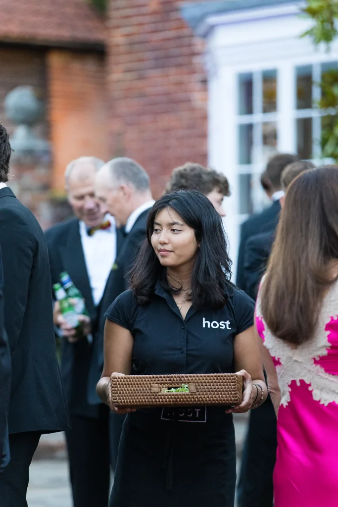 A server carries a tray between guests talking outside the red-brick house