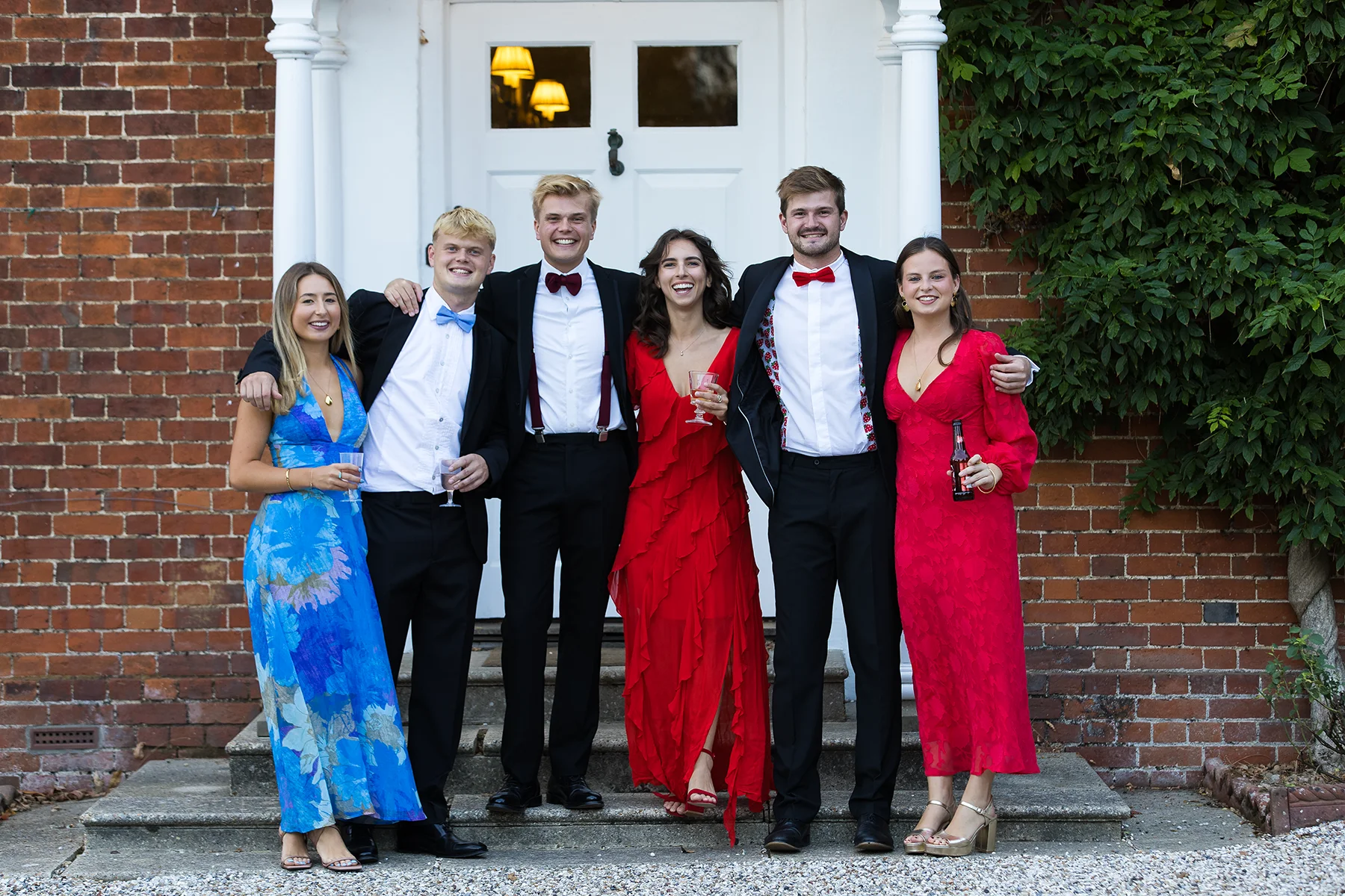 Six guests stand together in front of the white doorway and red-brick wall