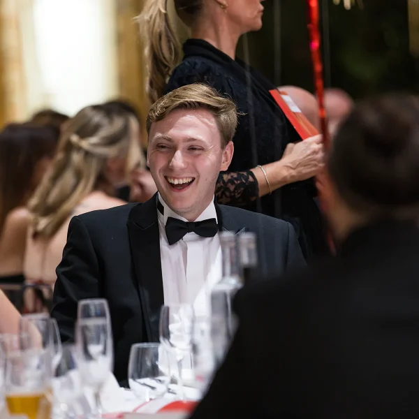A laughing man seated at dinner while a woman beside him looks towards him